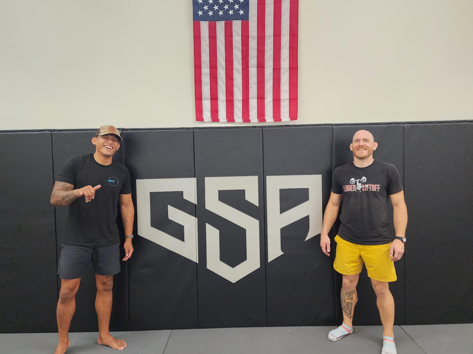 Members standing in front of the Grounded Strength Academy crest on the gym wall in Rio Rancho NM